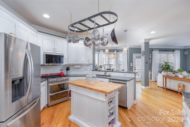 kitchen featuring crown molding, stainless steel appliances, a sink, butcher block countertops, and a peninsula