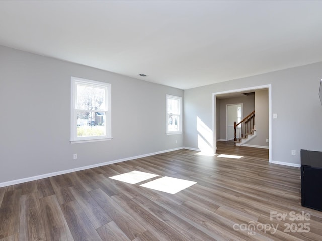 empty room featuring visible vents, stairway, wood finished floors, and baseboards