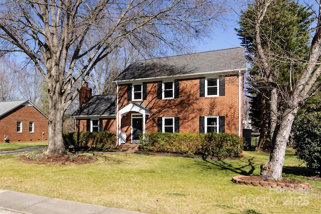 colonial house featuring brick siding, a chimney, and a front yard