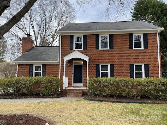 colonial house featuring brick siding, a chimney, and a front yard