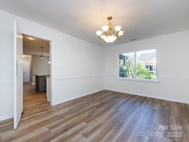 spare room featuring a chandelier, visible vents, light wood finished floors, and baseboards