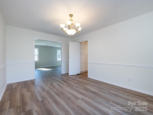 unfurnished room featuring a notable chandelier, wood finished floors, and baseboards