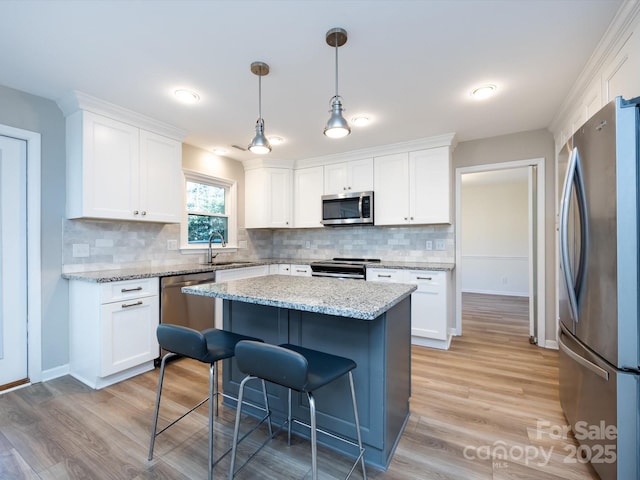 kitchen featuring light wood-type flooring, a sink, a kitchen breakfast bar, white cabinetry, and appliances with stainless steel finishes