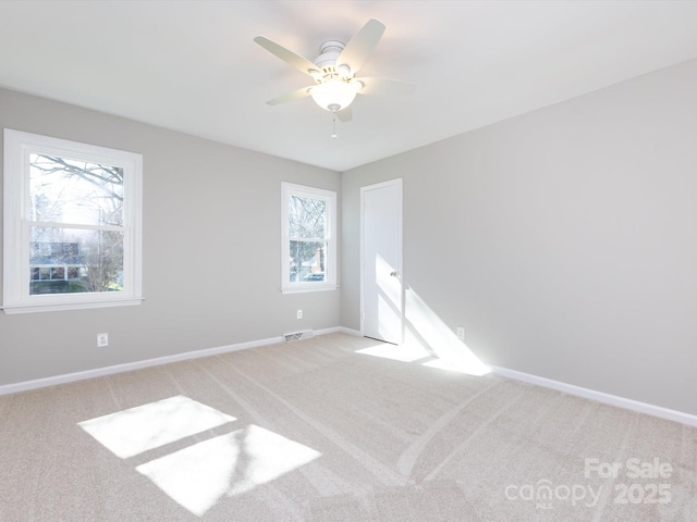 spare room with visible vents, light colored carpet, baseboards, and ceiling fan