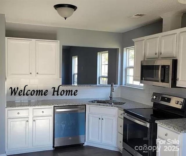 kitchen featuring backsplash, appliances with stainless steel finishes, white cabinetry, a sink, and light stone countertops