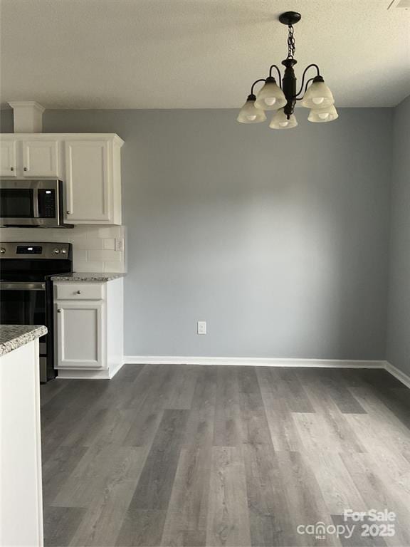 kitchen with decorative light fixtures, appliances with stainless steel finishes, dark wood-type flooring, white cabinetry, and baseboards