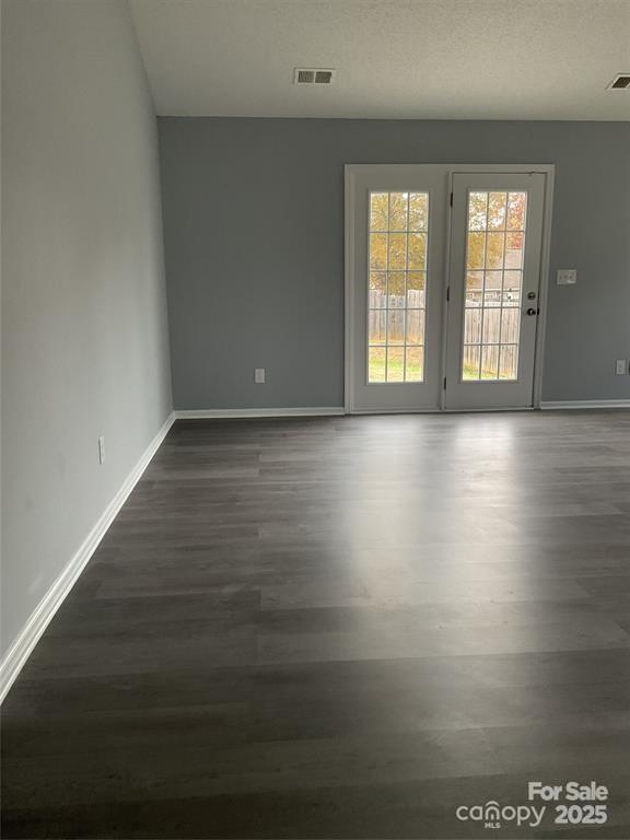 empty room with dark wood-style floors, a textured ceiling, visible vents, and baseboards