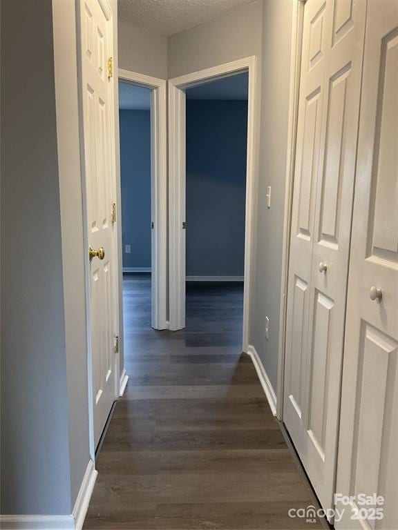 hallway featuring a textured ceiling, dark wood finished floors, and baseboards