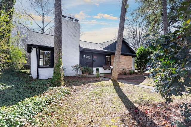 rear view of property with a shingled roof, brick siding, and a chimney