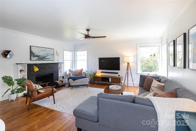 living room featuring baseboards, a ceiling fan, ornamental molding, wood finished floors, and a brick fireplace