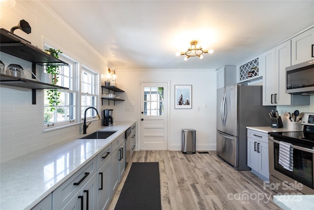 kitchen with crown molding, open shelves, stainless steel appliances, a sink, and light wood-type flooring