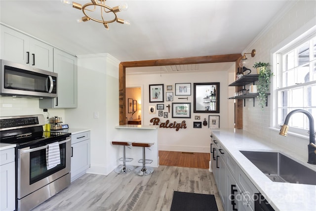 kitchen with tasteful backsplash, appliances with stainless steel finishes, light countertops, light wood-style floors, and a sink