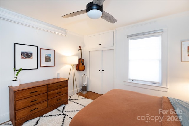 bedroom with baseboards, a ceiling fan, ornamental molding, light wood-style floors, and a closet