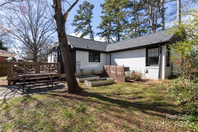 back of property with brick siding, a yard, a shingled roof, a deck, and a garden