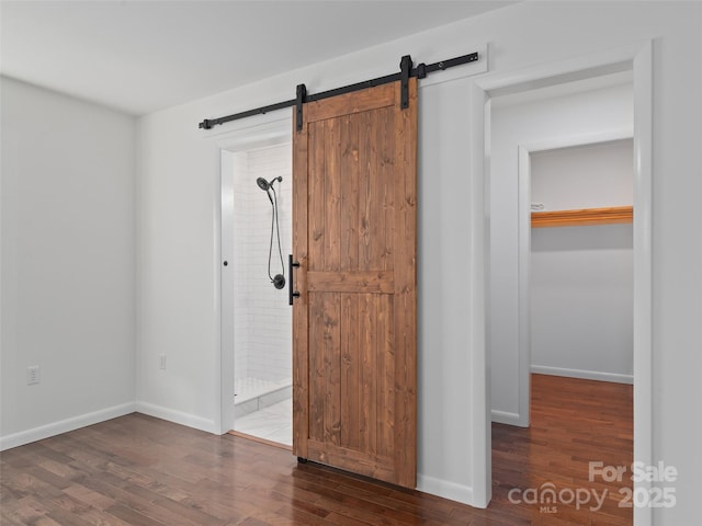 unfurnished room with a barn door, wood finished floors, and baseboards