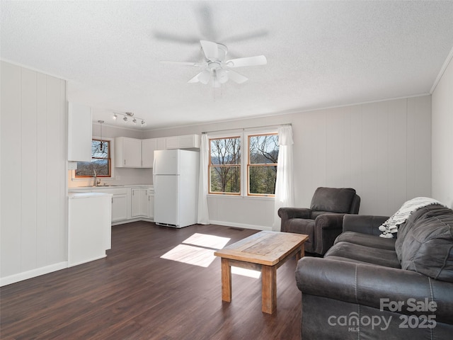 living room featuring a textured ceiling, ceiling fan, dark wood finished floors, and baseboards