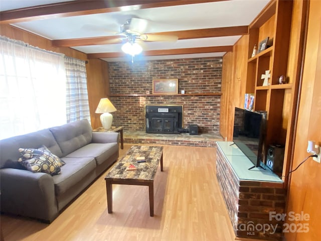 living area featuring a wood stove, beam ceiling, a ceiling fan, and wood finished floors