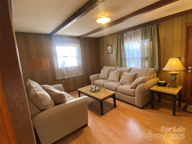 living area featuring a textured ceiling, wood walls, beamed ceiling, and light wood-style flooring