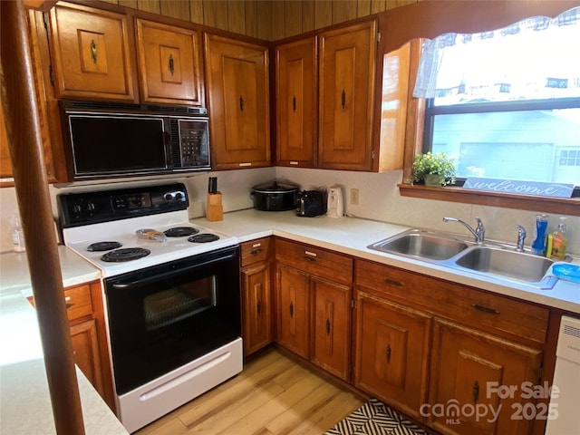 kitchen with black microwave, range with electric stovetop, a sink, light countertops, and brown cabinets