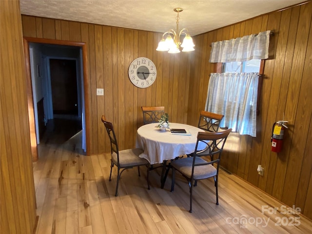 dining space with a textured ceiling, wood walls, light wood-style flooring, and an inviting chandelier