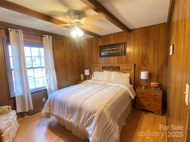 bedroom with ceiling fan, wood walls, beam ceiling, and light wood-style floors