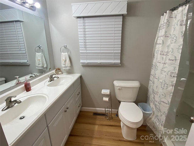 full bath featuring double vanity, wood finished floors, a sink, and toilet