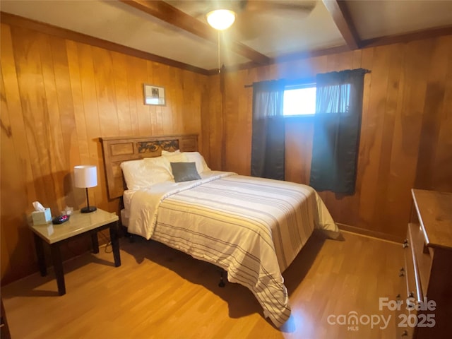 bedroom with ceiling fan, wood walls, baseboards, light wood finished floors, and beamed ceiling