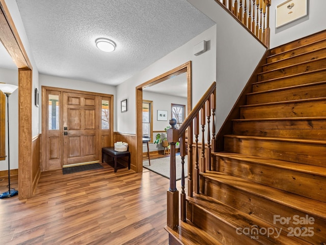 foyer entrance featuring a textured ceiling, stairway, wood finished floors, and wainscoting