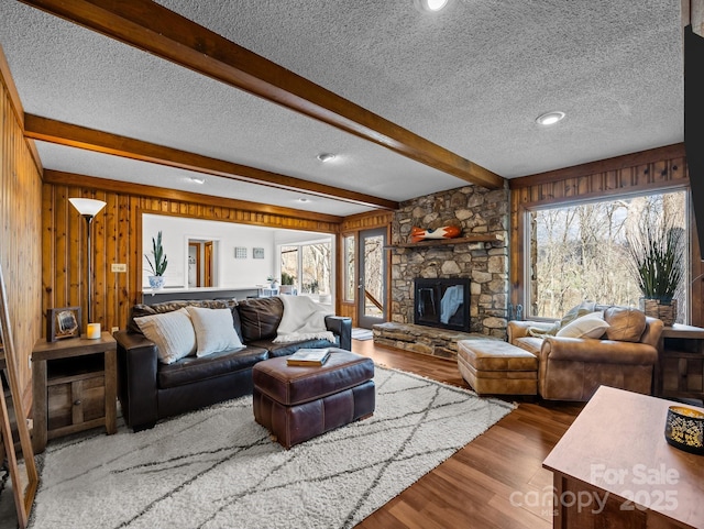 living room with wooden walls, beamed ceiling, a fireplace, wood finished floors, and a textured ceiling