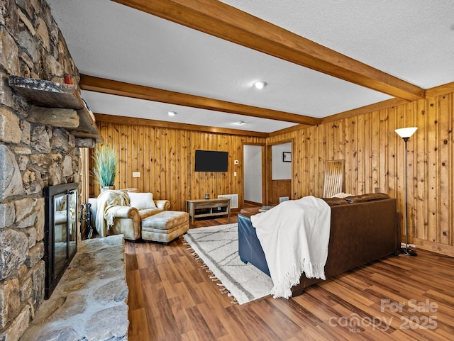 living room with beam ceiling, a textured ceiling, wood finished floors, and a fireplace