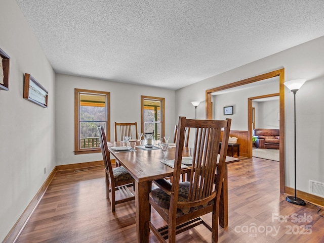 dining area with visible vents, wainscoting, a textured ceiling, and wood finished floors