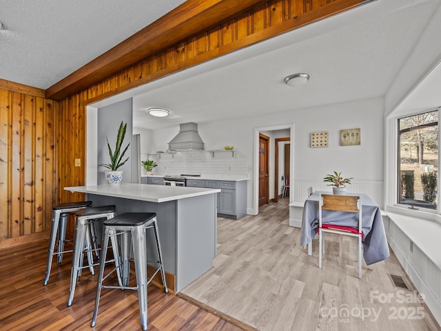 kitchen featuring visible vents, custom exhaust hood, light wood-style flooring, light countertops, and a kitchen breakfast bar