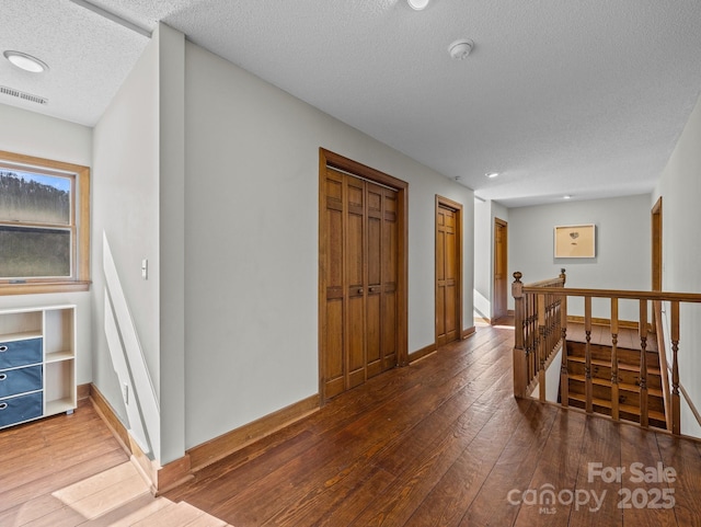 corridor featuring an upstairs landing, visible vents, a textured ceiling, and wood-type flooring