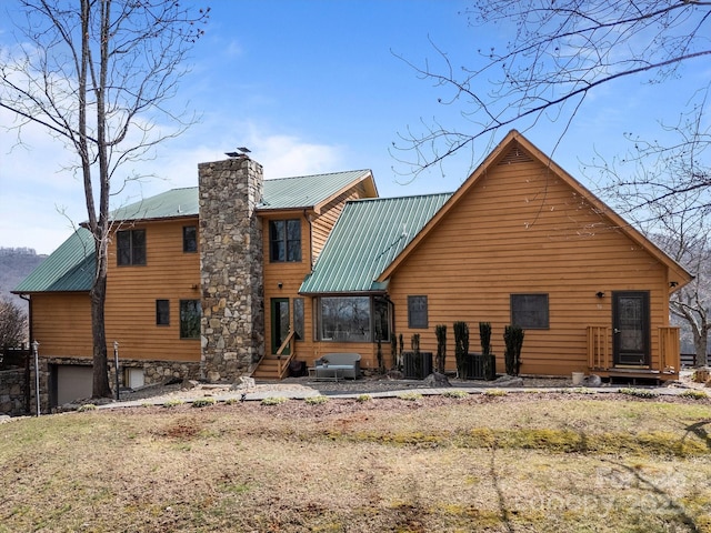 back of property with entry steps, central AC, a chimney, metal roof, and a garage