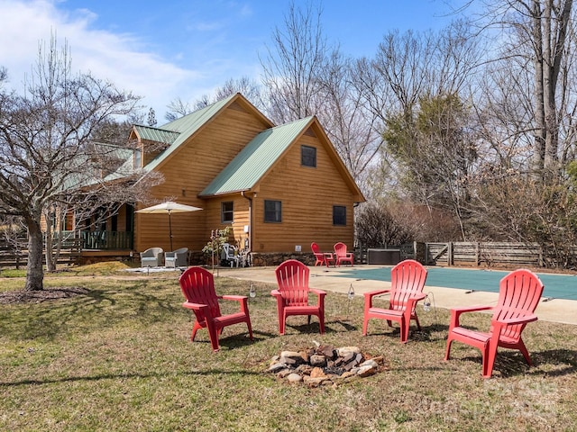 back of property with a covered pool, fence, an outdoor fire pit, metal roof, and a patio area