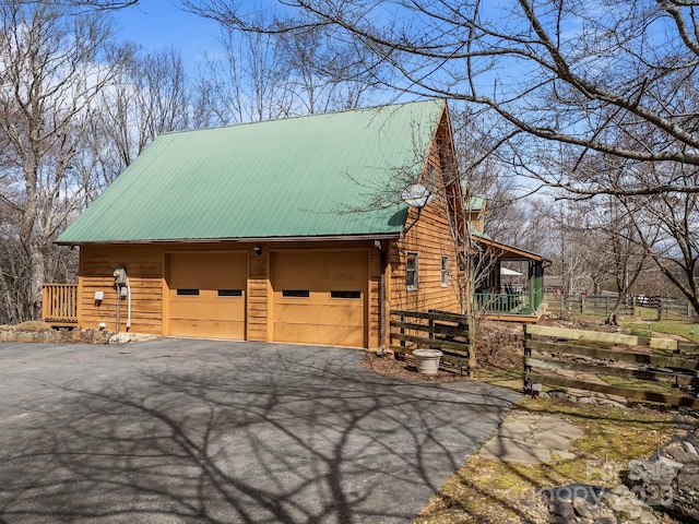 view of side of property featuring aphalt driveway, metal roof, and fence