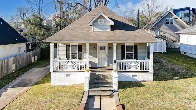 bungalow-style home featuring covered porch, roof with shingles, a front yard, and fence