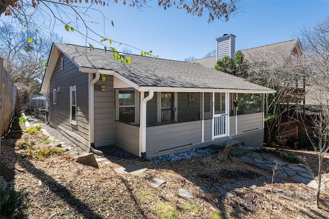 view of side of home with a shingled roof, a chimney, fence, and a sunroom