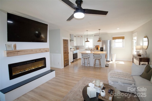 living area featuring light wood-type flooring, a wainscoted wall, and a glass covered fireplace