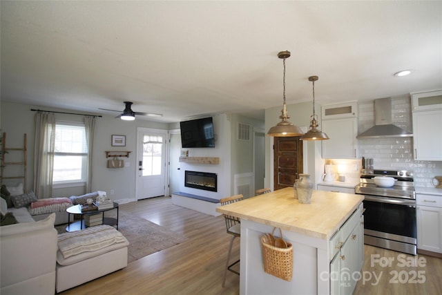 kitchen featuring wall chimney range hood, white cabinetry, open floor plan, and stainless steel range with electric cooktop