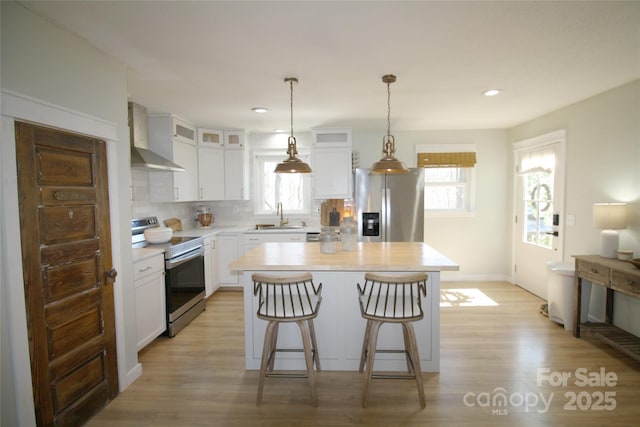 kitchen featuring a breakfast bar area, stainless steel appliances, light countertops, a sink, and wall chimney range hood