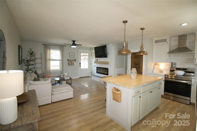 kitchen featuring electric stove, a glass covered fireplace, wall chimney exhaust hood, light wood-style floors, and white cabinetry