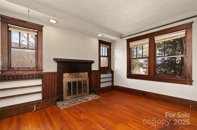 unfurnished living room featuring a wainscoted wall, a stone fireplace, and dark wood-style flooring