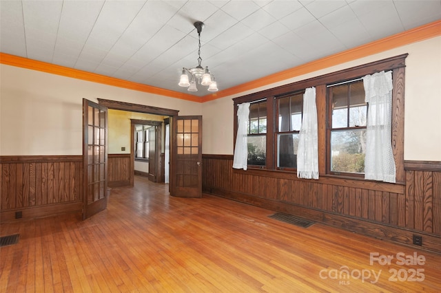 empty room featuring visible vents, wainscoting, ornamental molding, hardwood / wood-style floors, and an inviting chandelier