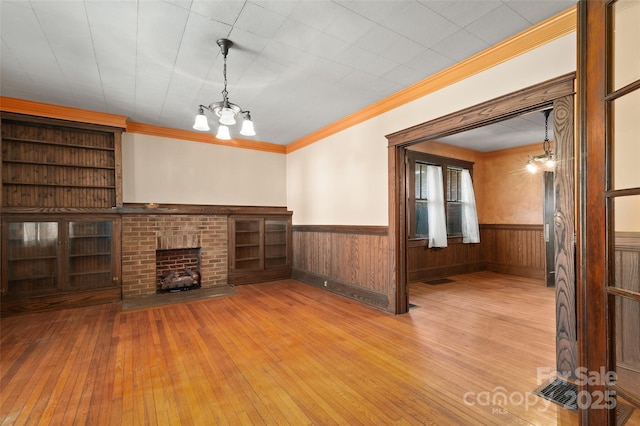 unfurnished living room with crown molding, wainscoting, a fireplace, and an inviting chandelier