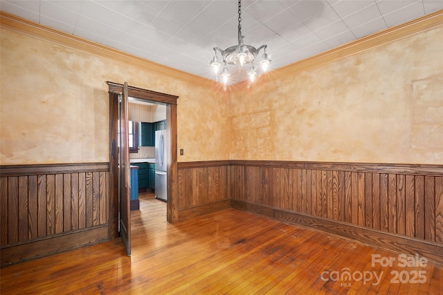 spare room featuring a wainscoted wall, crown molding, wood-type flooring, and a notable chandelier