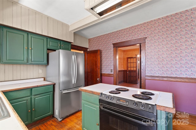 kitchen featuring black range with electric cooktop, light countertops, wainscoting, freestanding refrigerator, and wallpapered walls