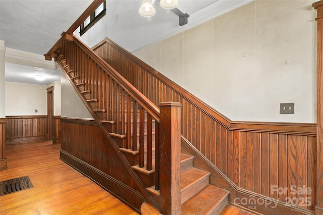 stairway with wooden walls, visible vents, wood finished floors, and wainscoting