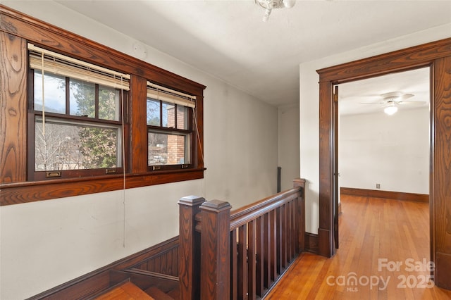 hall featuring light wood-style flooring, an upstairs landing, and baseboards