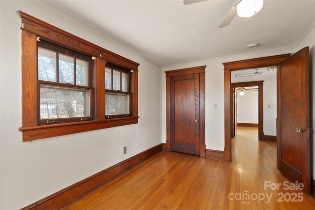 unfurnished bedroom featuring light wood-type flooring, baseboards, a ceiling fan, and ornamental molding